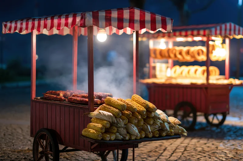 Two traditional turkish street food carts with grilled sausages and corn on cobblestone at night