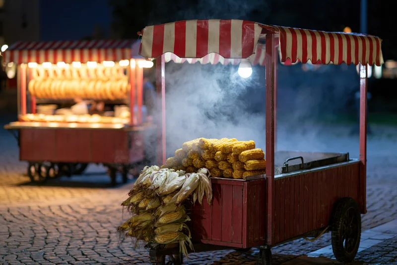 Steaming corn on a red striped cart on cobblestone at night