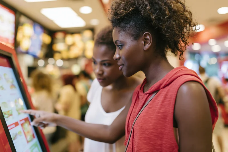 Two young women ordering at a self-service kiosk in a fast food restaurant