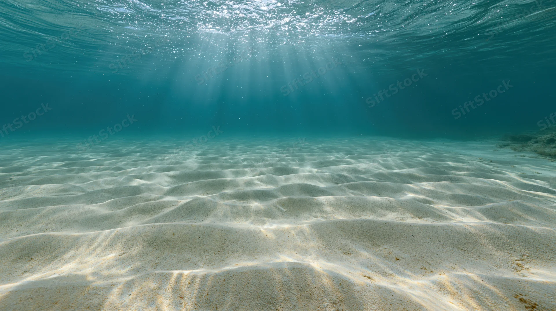 Underwater view of rippled sandy ocean floor with sunlight rays filtering through water surface