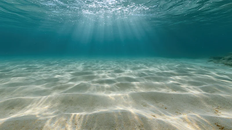 Underwater view of rippled sandy ocean floor with sunlight rays filtering through water surface