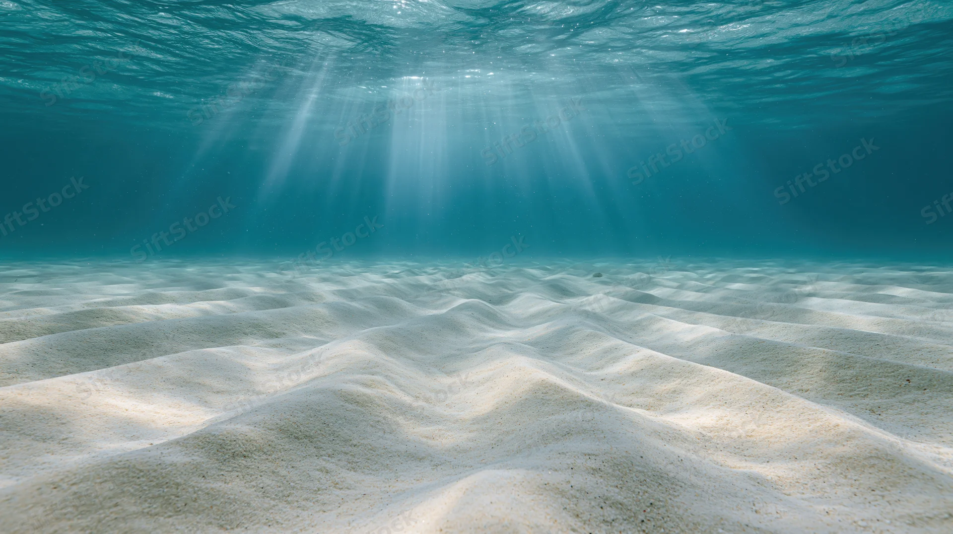 Rippled sandy ocean floor under sunlight beams from water surface