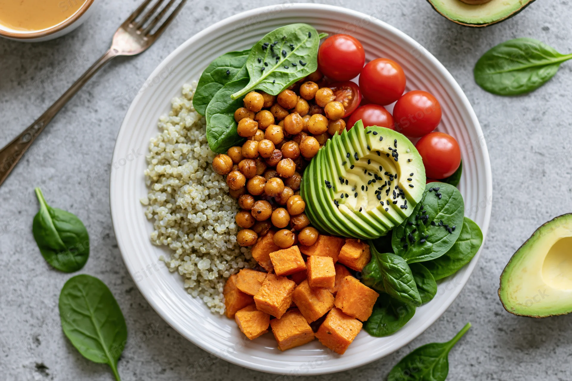 Vegan buddha bowl with quinoa, chickpeas, avocado, spinach, tomatoes and sweet potato on a white ceramic plate