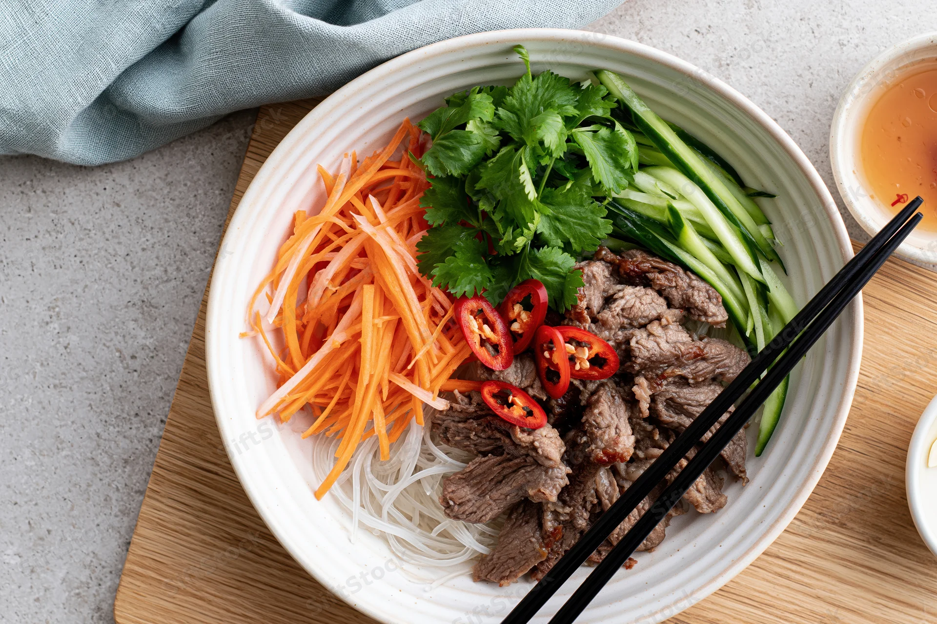 Vietnamese noodle bowl with sliced beef and shredded carrots on a wooden board