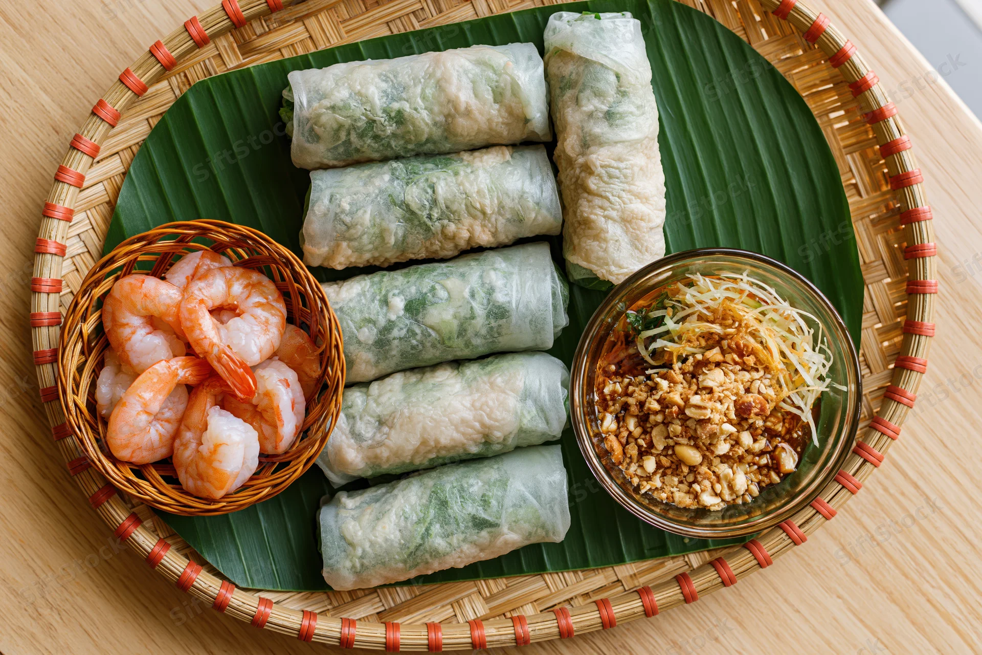 Vietnamese spring rolls arranged on a woven bamboo tray with shrimp and peanut sauce