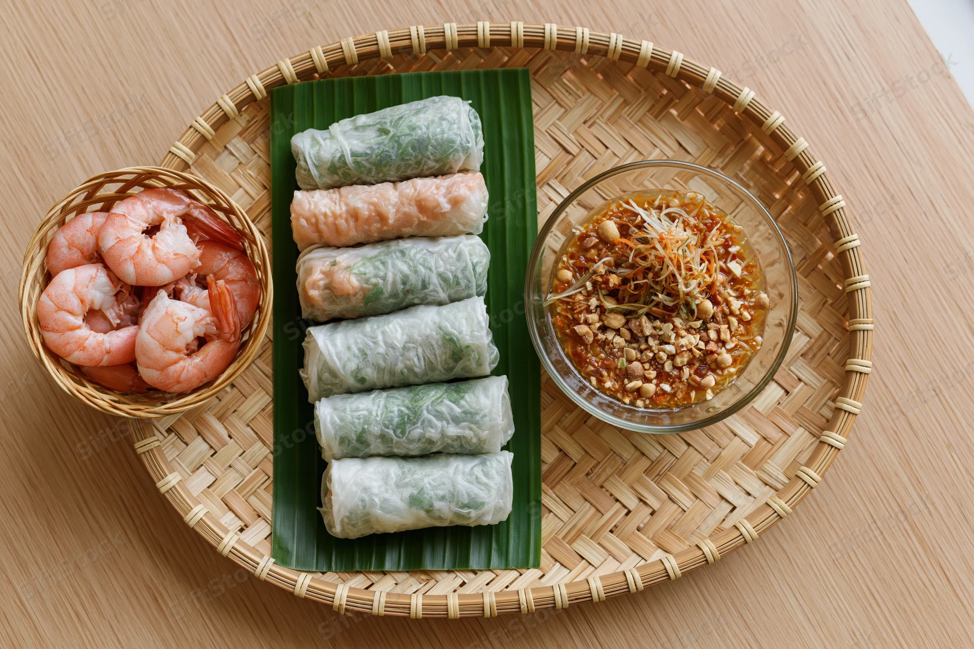 Vietnamese spring rolls arranged on a woven bamboo tray with shrimp and dipping sauce