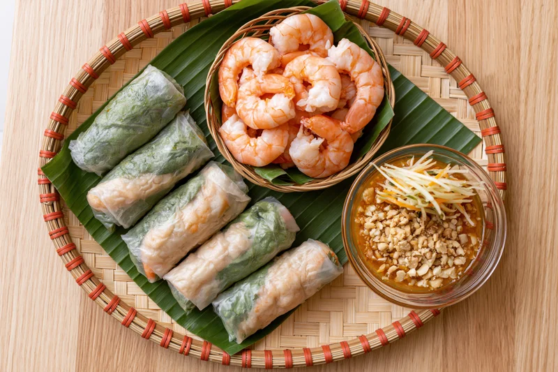 Vietnamese spring rolls with shrimp and peanut dipping sauce arranged on a woven bamboo tray over banana leaf