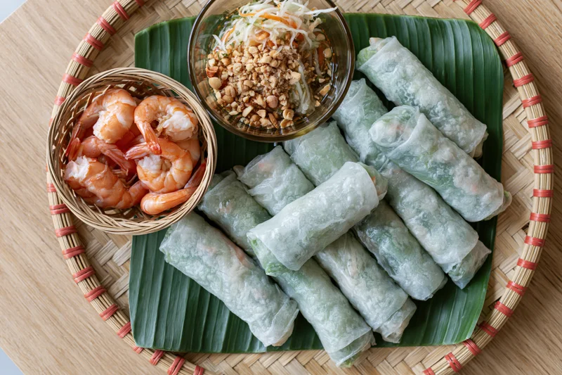 Vietnamese spring rolls with shrimp and peanut sauce on a woven bamboo tray lined with banana leaf