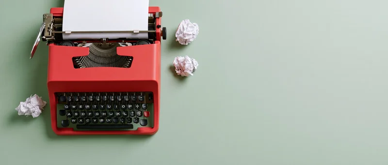 Red vintage typewriter with blank paper and crumpled drafts on mint green surface