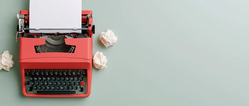 Red vintage typewriter with blank paper and crumpled drafts on a light green surface