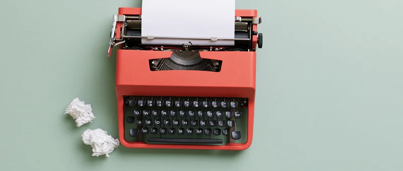 Vintage red typewriter with blank paper and crumpled drafts on mint green surface