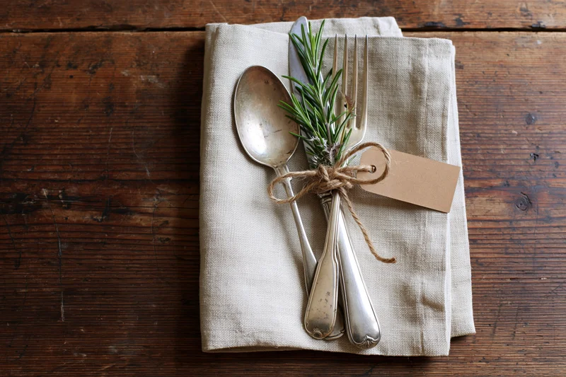 Vintage silver cutlery set tied with twine and rosemary on linen napkin on wooden table