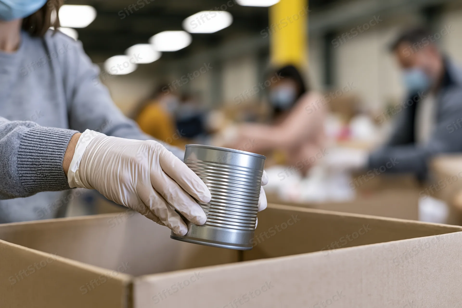 Volunteer placing a metal tin can into a cardboard box in a warehouse setting