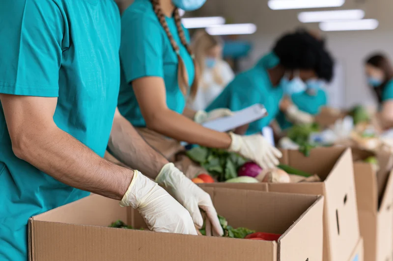 Volunteers sorting fresh vegetables into cardboard boxes at a food donation center