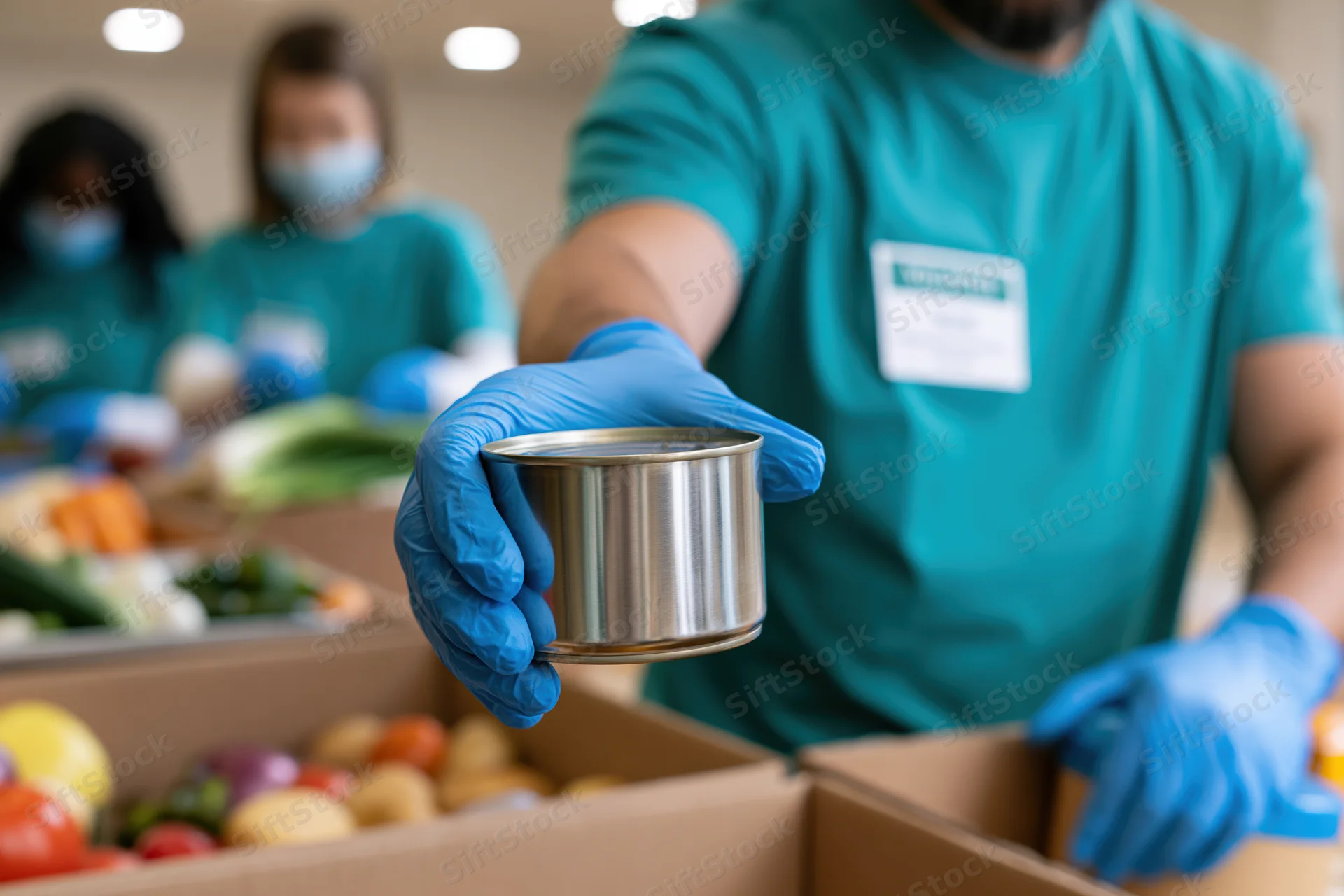 Volunteer holding a tin can over a box of groceries during food packing event