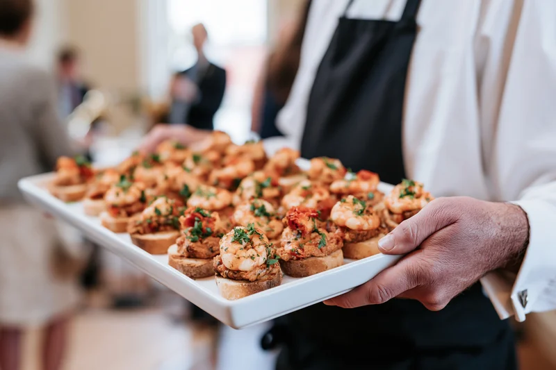 Waiter holding a white tray of shrimp canapes at a reception