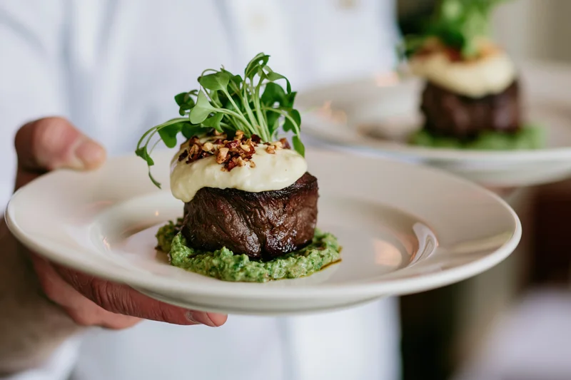 Waiter holding a plated steak dish with sauce and garnish in a fine dining setting