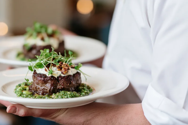 Waiter holding two plates with plated steak dishes in a fine dining restaurant