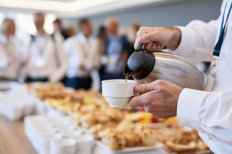 Man pouring coffee from a steel thermal carafe at a breakfast buffet