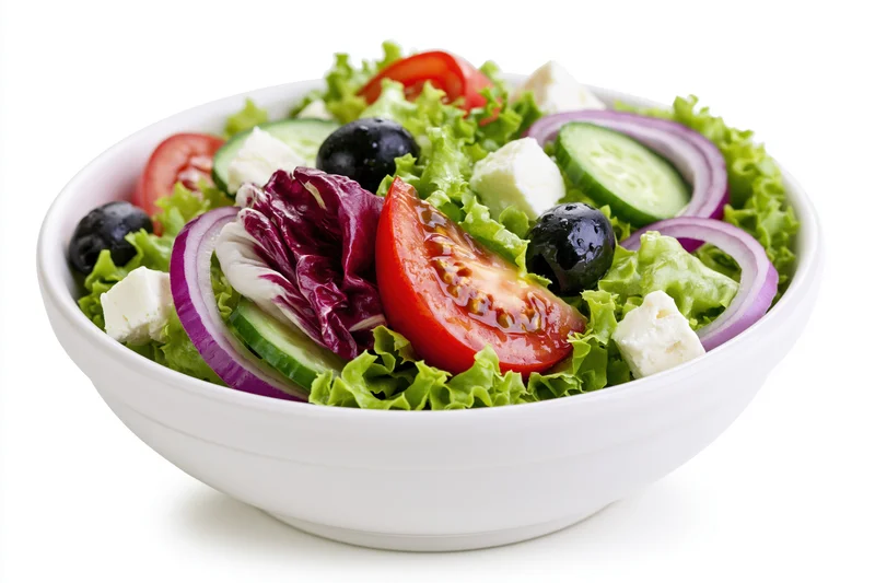 Greek salad in a white ceramic bowl with lettuce, tomato, cucumber, feta, olives and red onion