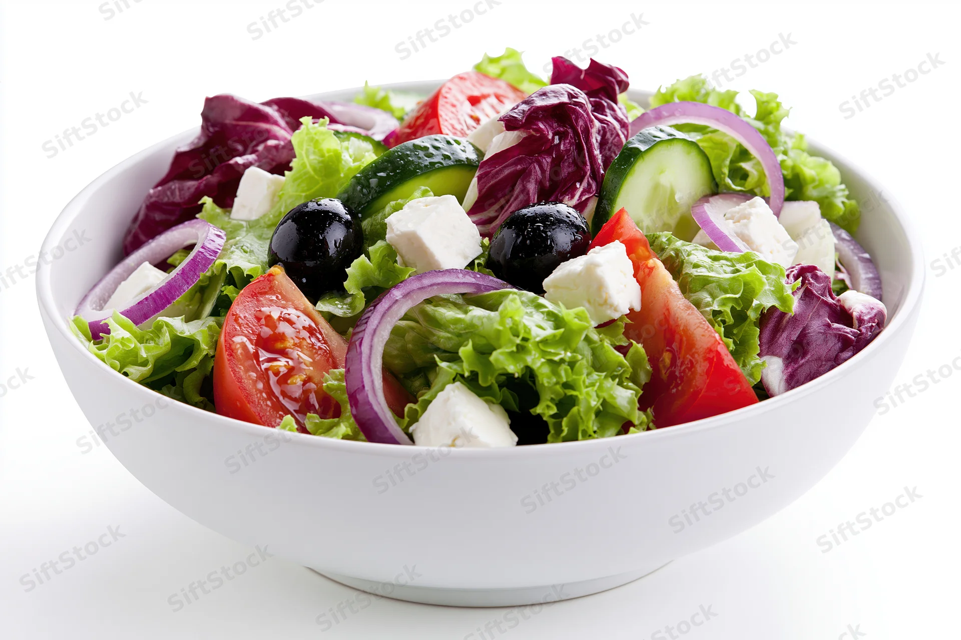 Greek salad with lettuce, tomato, cucumber, red onion, feta cheese and olives in a white ceramic bowl