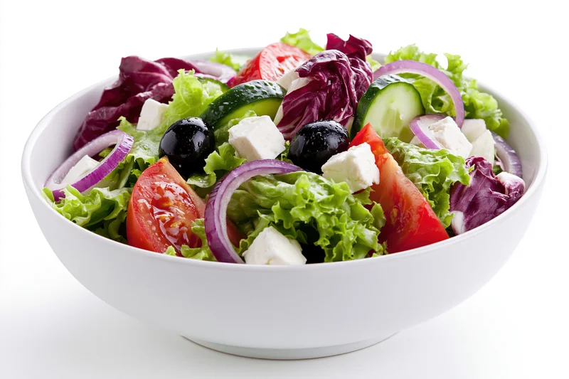 Greek salad with lettuce, tomato, cucumber, red onion, feta cheese and olives in a white ceramic bowl