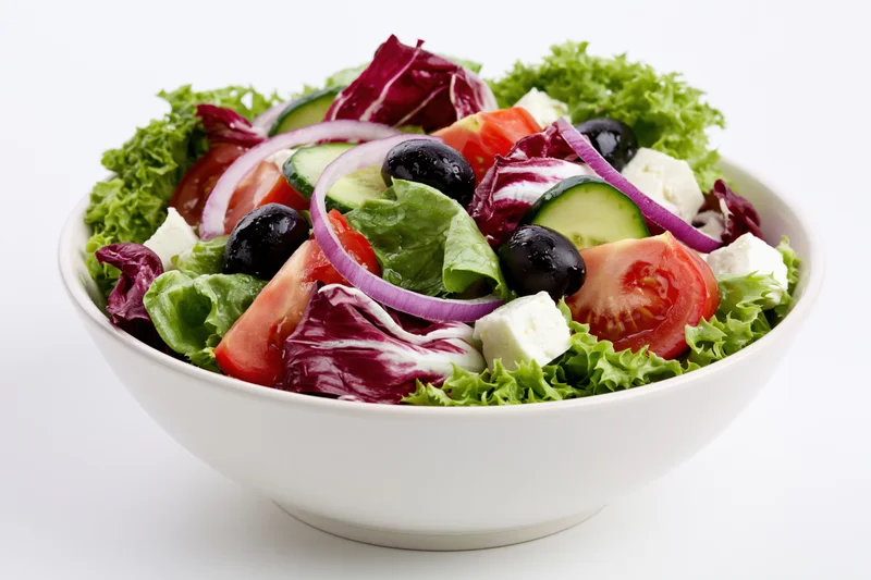 Greek salad with lettuce, tomato, cucumber, onion, black olives and feta cheese in a white ceramic bowl