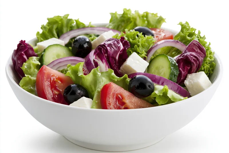 Greek salad with lettuce, tomato, cucumber, red onion, feta cheese and olives in a white ceramic bowl