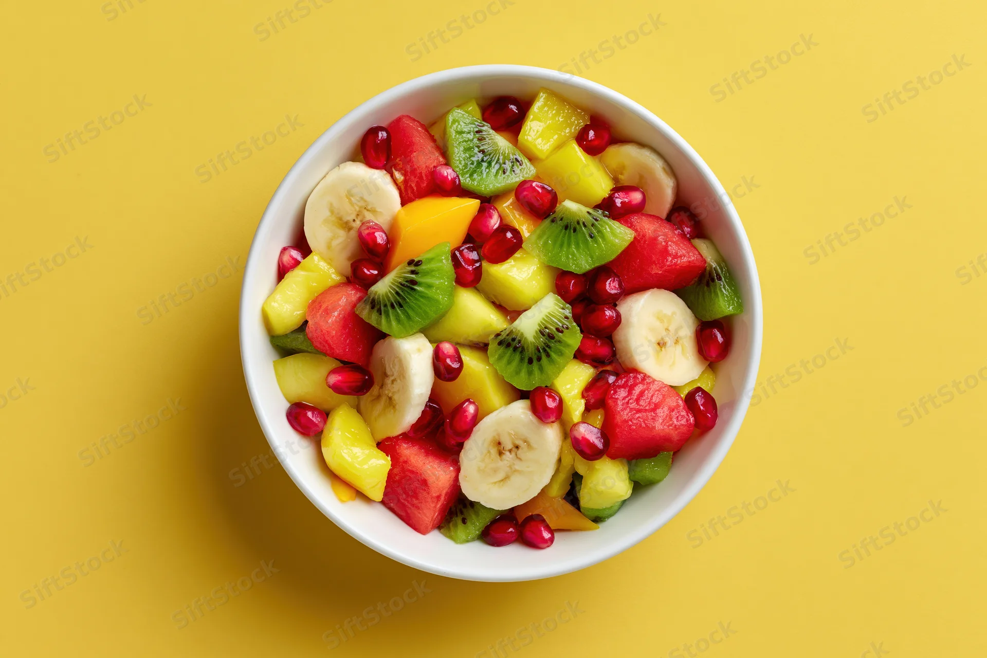 Mixed fruit salad in a white ceramic bowl on yellow background