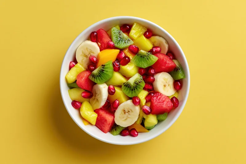 Mixed fruit salad in a white ceramic bowl on yellow background