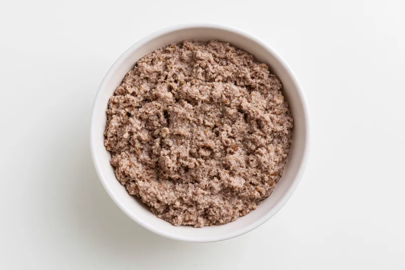 White ceramic bowl filled with wet canned dog food viewed from above on plain surface