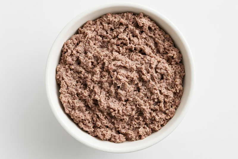 Wet canned dog food in a white ceramic bowl viewed from above on a plain surface