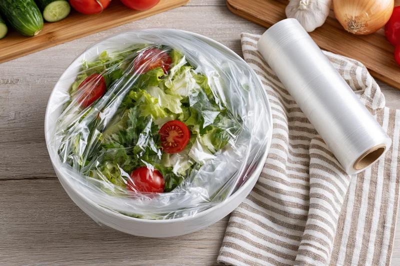 Fresh garden salad in white ceramic bowl covered with plastic wrap on wooden kitchen surface