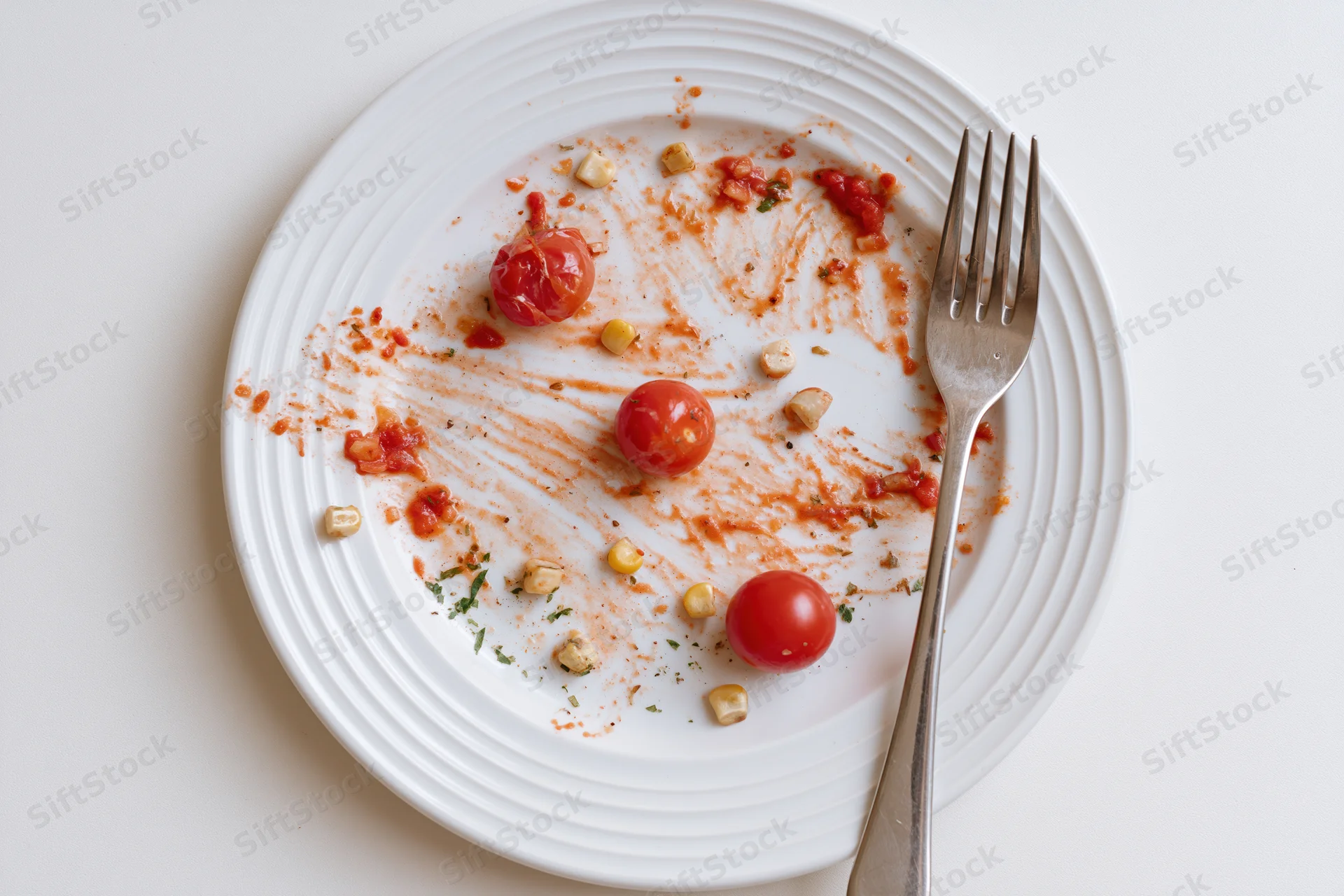 White ceramic plate with tomato sauce residue and fork after meal