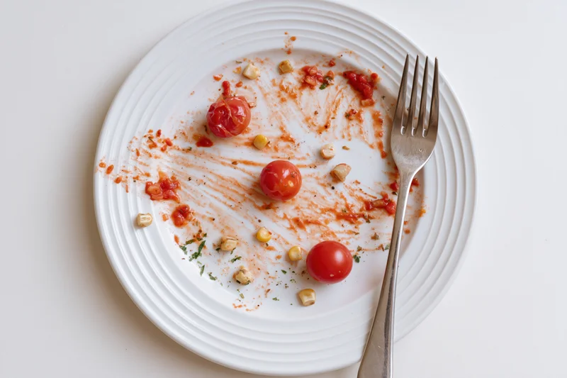 White ceramic plate with tomato sauce residue and fork after meal