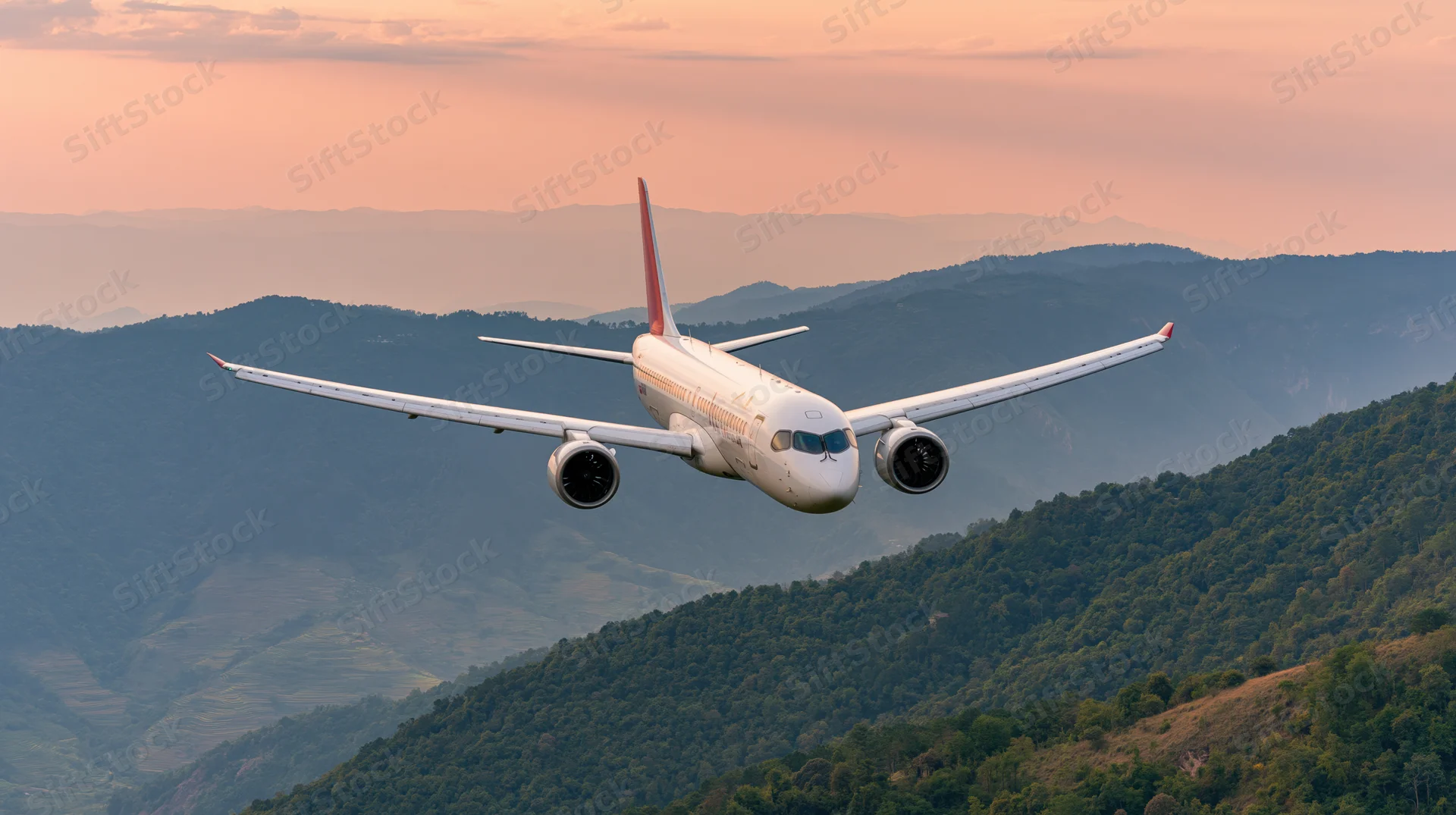 White commercial jet flying low over layered mountains at sunset