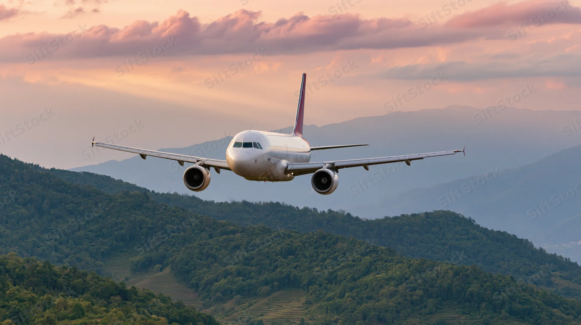 White commercial passenger jet flying low over layered mountains at sunset