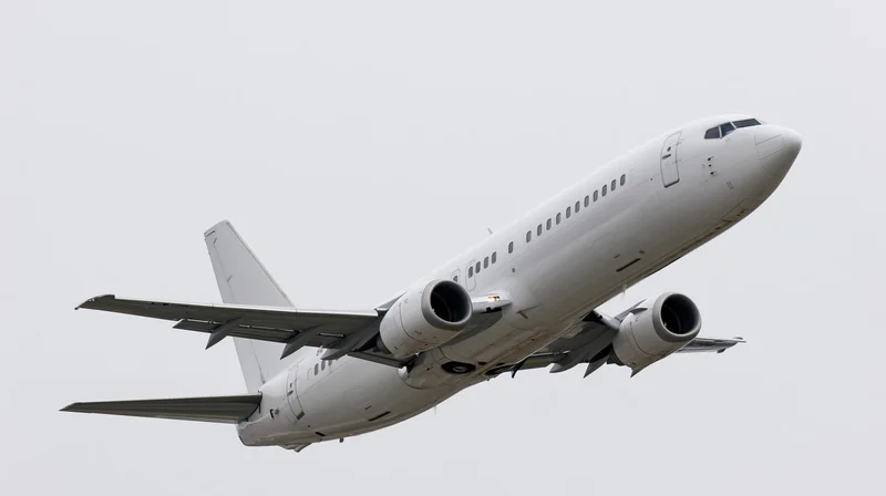 White narrow-body commercial passenger jet climbing steeply in overcast sky