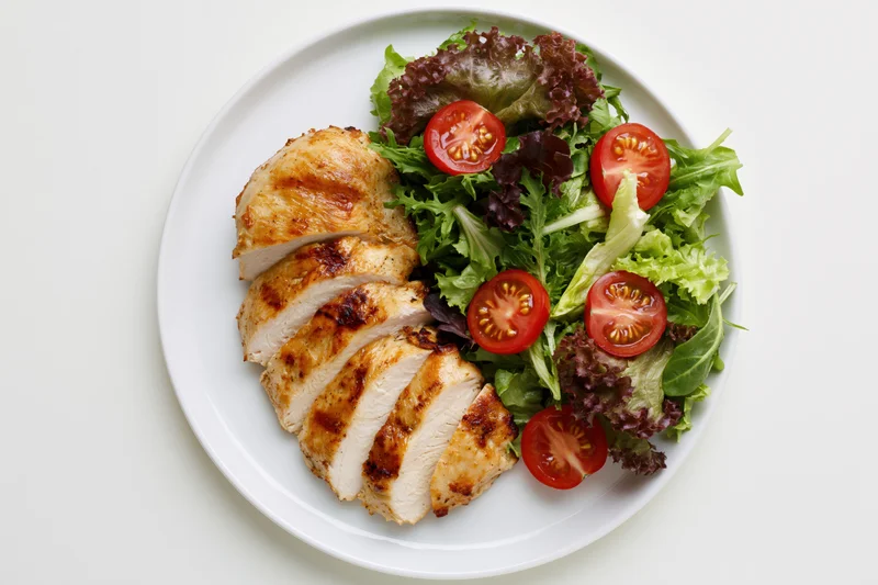 Grilled chicken breast sliced and served with mixed greens and cherry tomatoes on a white plate viewed from above