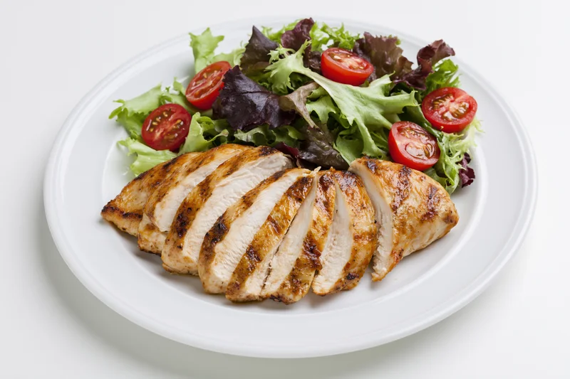 Grilled sliced chicken breast with mixed greens and cherry tomatoes on a white plate