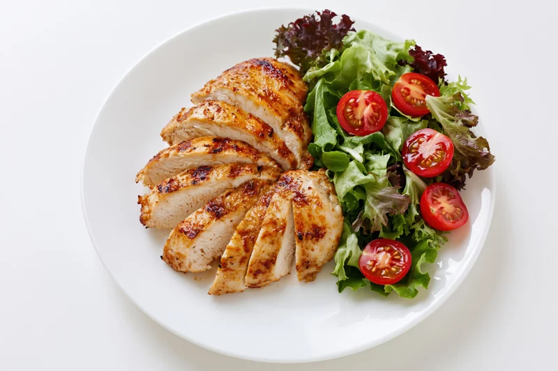 Grilled chicken breast sliced and served with mixed greens and cherry tomatoes on a white plate viewed from above
