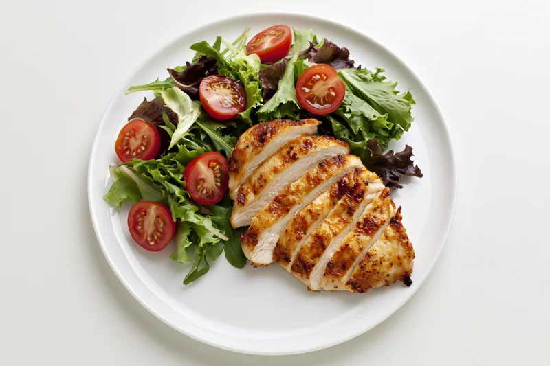 Grilled chicken breast with mixed greens and cherry tomatoes on a white plate viewed from above