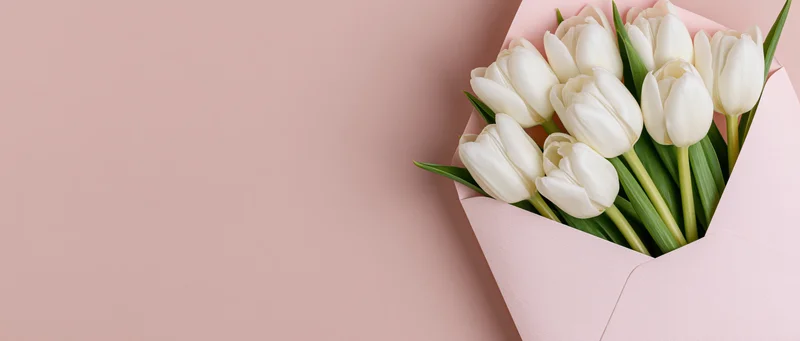 White tulips arranged in a pink envelope on a soft pink surface