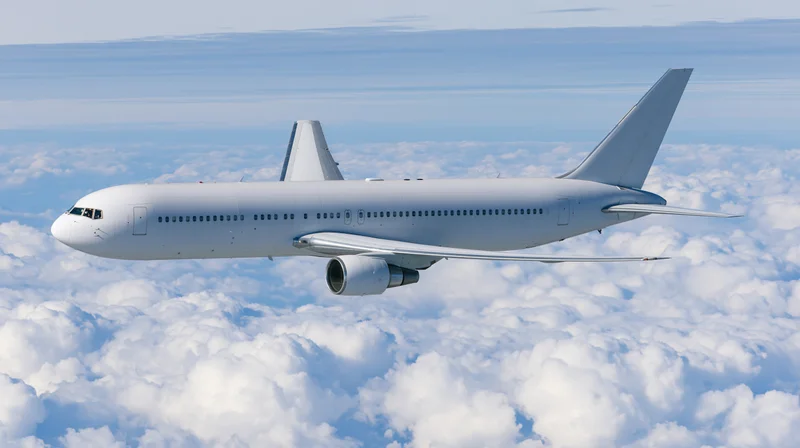 White wide-body commercial airliner flying above clouds in clear sky