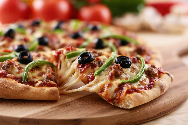 Pizza slice being pulled from whole pizza on round wooden cutting board