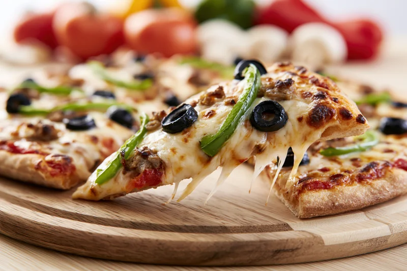 Slice of pizza with melted cheese and toppings lifted from wooden board