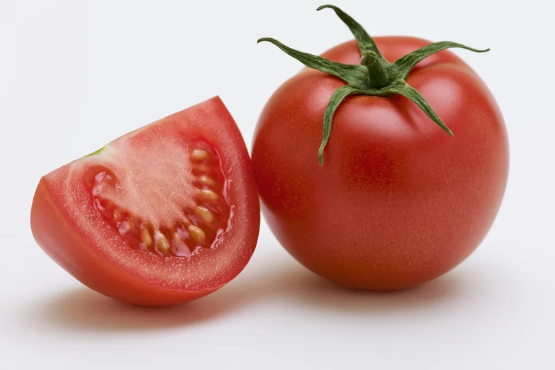 Whole ripe tomato with green calyx stem beside a sliced half on white background