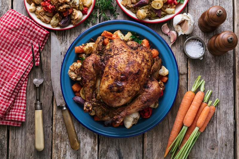 Whole roasted turkey on a blue enamel plate surrounded by vegetables and dinnerware on a rustic wooden table
