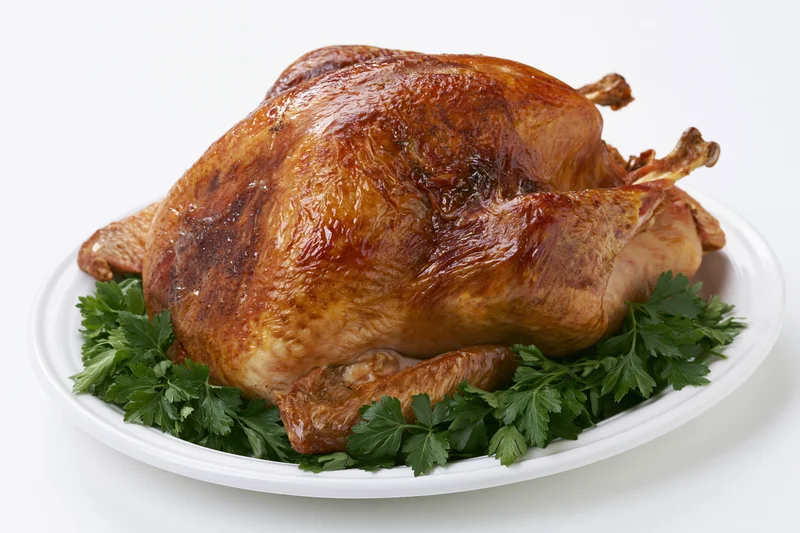 Whole roasted turkey on a white ceramic platter garnished with parsley