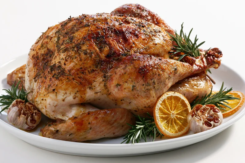 Whole roasted turkey on a white ceramic platter garnished with rosemary, orange slices, and garlic